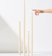 Four Hall of Flame Ivory Ultra-Bright LED Flameless Taper Candles of various heights stand upright on a white surface, while a hand with an extended finger reaches toward the tallest one. The background is plain white.