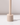 The Hall of Flame Sand Beige Wax Candle Holder, featuring a cylindrical shape and long vertical handle, stands upright on a white surface, casting a shadow to the right.