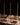 A formal dinner table features a white tablecloth, three Hall of Flame ULTRABRIGHT™ LED Flameless Taper Candles in gold holders, glassware, cutlery, and hardcover books with menus at each place. The softly lit background is dark.