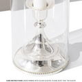 The Short | Antique Gold Holder by Hall of Flame features a white candle in an antique gold alloy base with a clear glass sleeve, recalling vintage charm. Below on the white surface, black text advises on stability and sticky dots for outdoor/tall use.