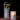 Two Hall of Flame Spike Hand Blown Vases sit on a brown surface against a dark backdrop—one holds dark purple and green flowers, the other glows warmly with a lit candle inside.