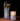 Two Hall of Flame Spike Hand Blown Vases sit on a brown surface against a dark backdrop—one holds dark purple and green flowers, the other glows warmly with a lit candle inside.