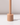 The Venti Brown Wax Candle Holder by Hall of Flame features a cylindrical beige design with a vertical rod on a matching base, casting a shadow on white against a light background.