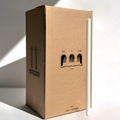 A tall white candle stands next to a large Hall of Flame box labeled “Bulk Candles | Wholesale by-the-box – 60 PC XXL” with “THIS WAY UP” arrows, ideal for wholesale candles Australia. Light from the left casts shadows.