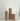 The Hall of Flame Pillars in Glass Vase Trio features three beige pillar candles of different heights arranged in clear glass holders on a white surface against a white wall.