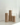 The Hall of Flame Pillars in Glass Vase Trio features three beige pillar candles of different heights arranged in clear glass holders on a white surface against a white wall.