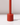 The Hall of Flame Poppy Red Wax Candle Holder, a tall cylindrical piece, stands upright on a white surface casting a small shadow to the right. Its plain light background highlights its sustainable plant-based wax design.